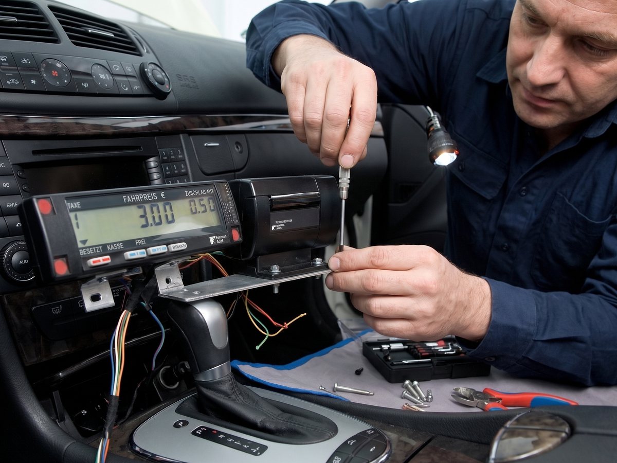 Techniker beim Einbau eines Taxameters in das Armaturenbrett eines Taxis